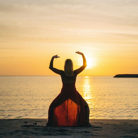 Woman practicing a gentle yoga stretch outdoors at sunset.